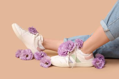 Bej arka planda Eustoma çiçekleri olan spor ayakkabılı genç kadın bacakları.