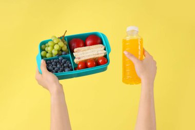 Okulun beslenme çantalı kadın elleri ve sarı arka planda bir şişe meyve suyu.