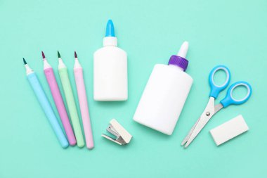 Turkuaz arka planda bir şişe tutkal, makas ve keçeli kalemler. İpucu görünümü