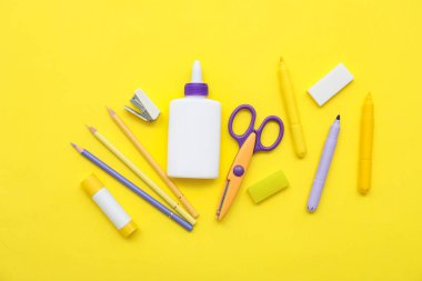 Sarı arka planda bir şişe tutkal, makas ve kalem. Üst görünüm