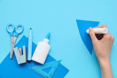 Yapıştırıcı çubuğu, zımba ve mavi arka planda keçeli kalemle kadın eli. Üst görünüm