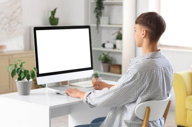 Genç adam evdeki masada bilgisayar kullanıyor.