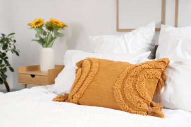 Yumuşak yastıklı rahat bir yatak ve yatak odasındaki komodinin üzerinde güzel ayçiçekleri.