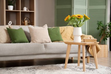 Gri kanepesi ve kahve masasında ayçiçekleri olan şık bir oturma odası.