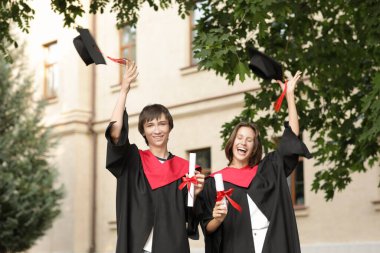 Açık havada diplomalı mutlu mezun öğrenciler.
