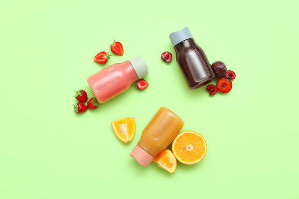 Спортивные бутылки свежего сока с различными фруктами на зеленом фоне
