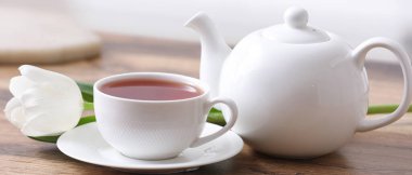 Çaydanlık, bir fincan sıcak içecek ve lale masada, yakın plan.