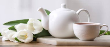 Çaydanlık, bir fincan sıcak içecek ve masada laleler.