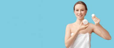 Açık mavi arkaplan üzerinde kozmetik krem dolu kavanozları olan genç bir kadın.