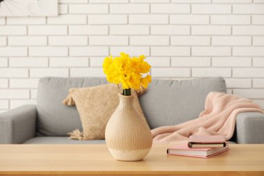 Oturma odasındaki masa üzerinde narsisli çiçekler ve kitaplar olan vazo.