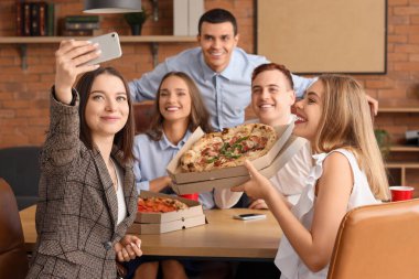 Pizzalı bir grup genç iş arkadaşı ofis partisinde selfie çekiyor.