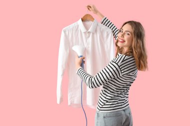 Pembe arka planda modern giysi buharı olan güzel, genç bir kadın.