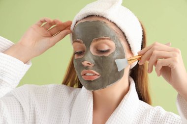 Uygulamalı yüz maskesi ve yeşil arka planda fırçası olan genç kadın, yakın plan.