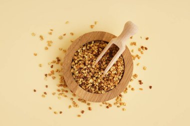 Tahta kase ve kepçeyle bej arka planda çiğ karabuğday taneleri.