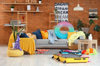 Oturma odasının içinde bir sürü kıyafet ve yerde açık bavullar var. Seyahat kavramı