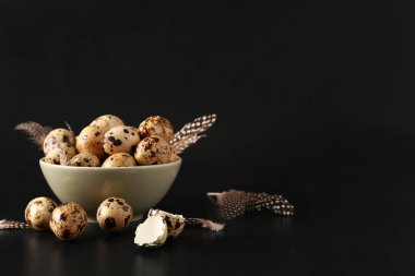 Siyah arka planda taze bıldırcın yumurtası ve tüyleri olan bir kase.
