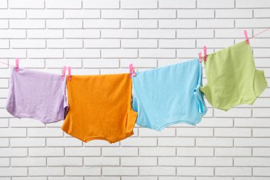 Temiz giysiler ipte asılı, tuğla duvara karşı.
