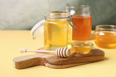 Kavanoz ve bir kase tatlı bal, sarı masada da kepçe.