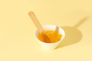 Soluk sarı arka planda şekerli macun ve spatula ile kase