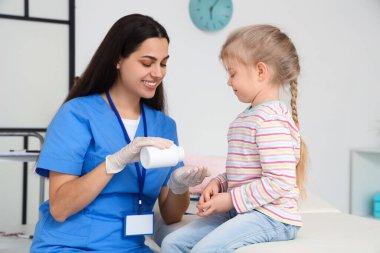 Kadın çocuk doktoru klinikteki küçük kıza ilaç veriyor.