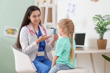 Klinikteki küçük kıza astım spreyini gösteren kadın bir çocuk doktoru.
