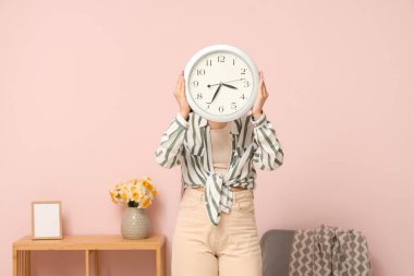 Güzel bir odada rafların yanında saati tutan genç bir kadın.