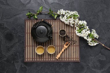 Bardaklı çaydanlık, bir kaşık kuru çay ve siyah grunge arka planda çiçekler.