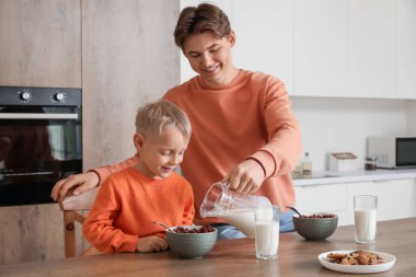 Küçük oğluyla mutlu bir baba mısır gevreği yiyor ve kahvaltıda süt içiyor.