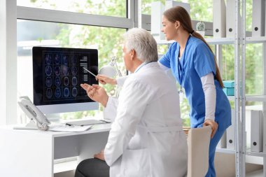 Hemşiresi olan olgun bir doktor klinikteki bilgisayar ekranında MRI taraması yapıyor.