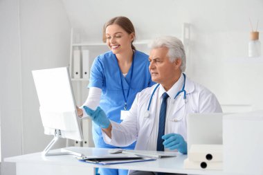 Klinikteki masada bilgisayarla çalışan olgun doktor ve hemşire.