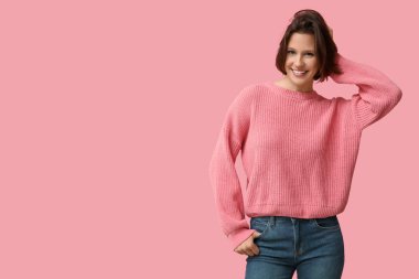 Pembe arka planda şık süveter giyen mutlu genç kadın.