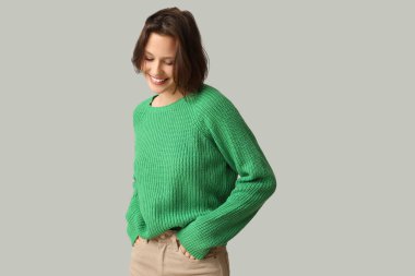 Gri arka planda zarif yeşil süveter giyen güzel genç bir kadın.