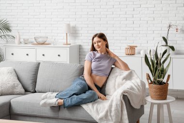 Oturma odasındaki rahat kanepede dinlenen güzel genç bayan.