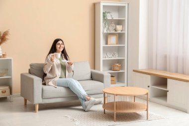 Gri koltukta oturan fincanlı güzel genç bayan şık oturma odasında.