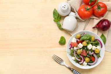 Tahta arka planda sağlıklı sebze salatası, çatal ve malzemelerle dolu bir kâse.