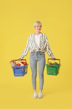 Sarı arka planda alışveriş sepetleri olan genç bir kadın.