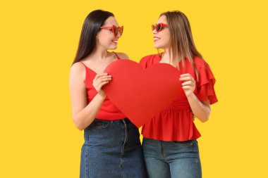 Sarı arka planda kağıt kalpli güzel bir lezbiyen çift.
