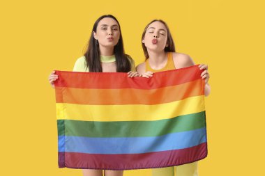 Sarı arka planda öpüşen LGBT bayrağı taşıyan güzel lezbiyen çift.