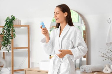 Evdeki banyoda deodorantı olan güzel, genç ve mutlu bir kadın.