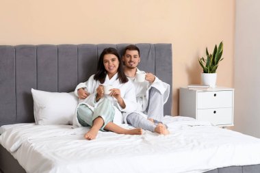 Yatak odasında kahve içen mutlu genç çift.