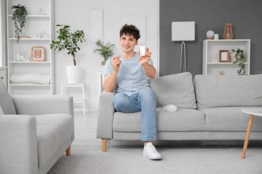 Evdeki kanepede oturan glukometresi ve tükenmez kalemi olan diyabetik genç adam.