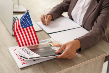 Amerikan bayrağı ve dergileriyle genç ve güzel Afro-Amerikan iş kadını ofiste oturuyor.