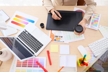 Tabletli ve kahveli kadın grafik tasarımcısı ofiste çalışıyor.
