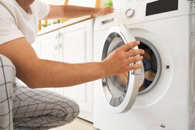 Çamaşır odasında çamaşır makinesi kullanan genç adam.
