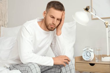 Yatak odasında çalar saatin yanında oturan genç adam. Uykusuzluk kavramı