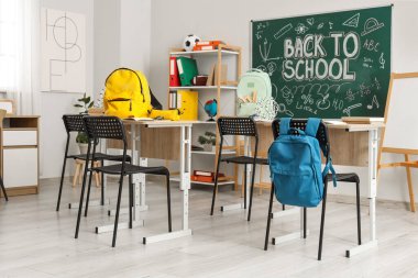 Işık sınıfında okul sıraları, sırt çantaları ve karatahta