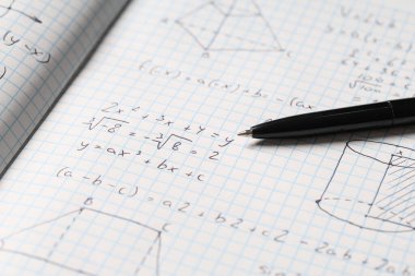 Arka plan olarak el yazısıyla yazılmış matematik formülleri ve kalemi olan kopya defteri, yakın plan