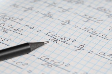 Arka plan olarak el yazısıyla yazılmış matematik formülleri ve kalemi olan kopya defteri, yakın plan