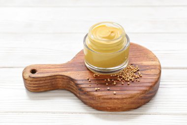 Tahtada hardal kavanozu ve beyaz ahşap arka planda tohumlar var.