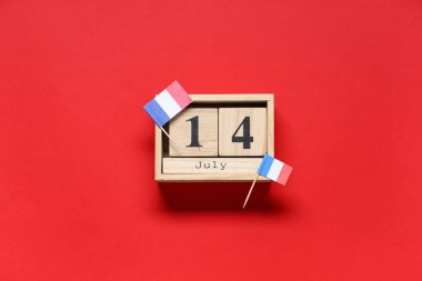 14 Temmuz tarihli küp takvimi ve kırmızı arka planda Fransız bayrakları. Bastille Günü kutlamaları